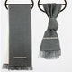 Gray woven towels with fringed edges hang on round hooks. One towel is flat, while the other is knotted. Both feature a decorative embroidered pattern.