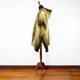 A mannequin displays a draped, multi-toned shawl with gold and beige hues and intricate patterns. It stands in a room with wooden flooring against a plain white wall.