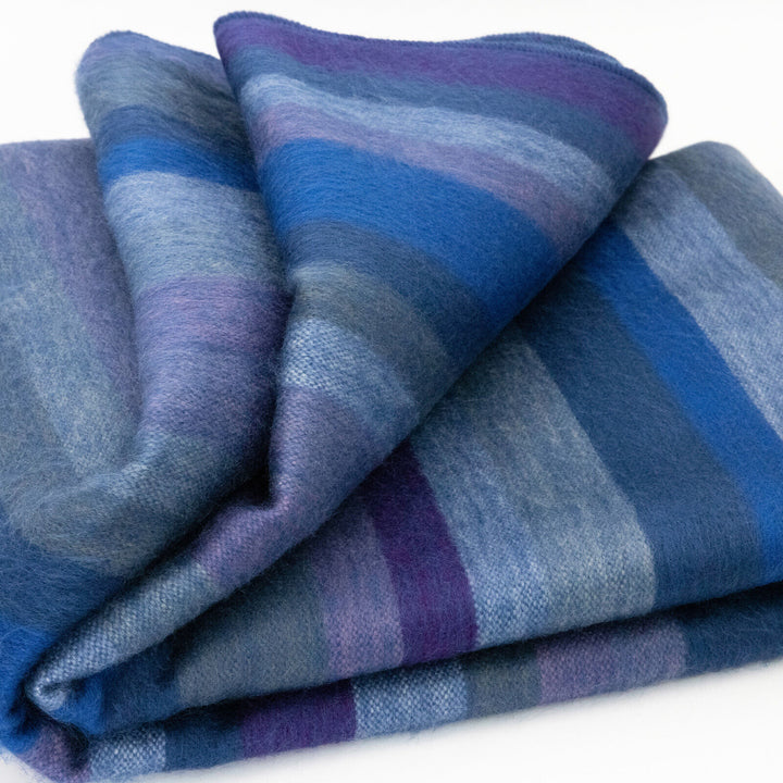 Morona baby alpaca wool blanket – a folded blanket displays stripes in shades of blue, purple, and gray, lying on a flat surface