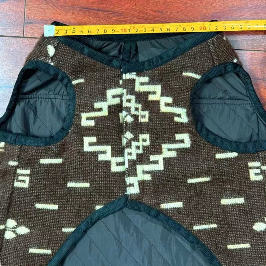 A brown woven vest featuring geometric patterns, displayed flat on a wooden floor with a yellow measuring tape stretched across its top, reading to 21 inches.