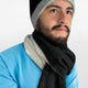 A person wears a black and gray beanie and scarf, with a blue shirt, looking slightly upward in front of a plain white background.