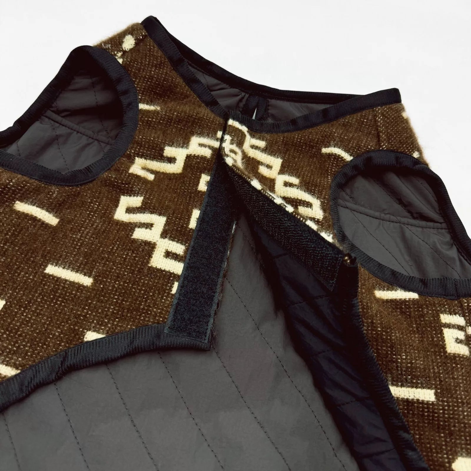 Quilted vest with beige geometric patterns on brown fabric, featuring black trim and Velcro closure, lying against a plain white background.