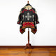 A colorful poncho with geometric patterns hangs on a wooden stand, set against a white wall and hardwood floor.