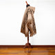 A brown and patterned poncho drapes over a mannequin. The poncho features geometric designs and fringe, set against a white background and positioned on a wooden floor.