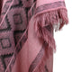 A pink fabric with black geometric patterns hangs, featuring a fringed edge, suggesting a shawl or blanket in a close-up view.