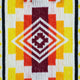 A woven textile features a central diamond pattern in white and maroon, surrounded by vertical stripes in red, orange, and yellow, with a black border, creating a vibrant geometric design.