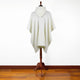 A white hooded poncho drapes over a wooden mannequin stand, positioned on a polished wooden floor against a plain white wall.