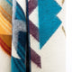 A close-up of a colorful woven fabric, featuring geometric patterns in teal, blue, orange, and purple, showcasing a textured surface with visible stitching along one edge.