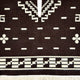 Kids Clint Eastwood alpaca wool poncho – a textile features geometric white motifs on a dark background, with patterns including lines, squares, and floral designs. The bottom edge has a checkered border with fringe details