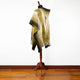 A shawl with intricate golden patterns drapes over a mannequin, set against a plain white background with a wooden floor beneath.