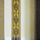 A woven textile features vertical stripes in earthy tones. The center stripe has a repeated geometric pattern in yellow and black, surrounded by gradient colors, giving a warm texture.