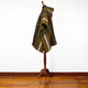 A multicolored poncho with geometric patterns draped on a wooden mannequin stand in a room with wooden flooring and a plain white wall.