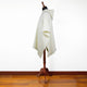 A cream-colored poncho with a hood drapes over a wooden mannequin, standing on a polished hardwood floor against a plain white background.