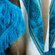A vibrant blue fringe decorates a patterned fabric, with intricate designs blending brown, cream, and teal hues, creating a visually textured and cozy textile.