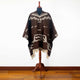 Kids Clint Eastwood alpaca wool poncho – a brown poncho with white geometric patterns is displayed on a wooden mannequin stand, set against a plain white background on a hardwood floor