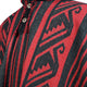 A fabric garment features bold black and red geometric patterns with button details. The design includes intricate arrow-like and wavy shapes, creating a dynamic visual against the textured background.