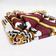 A folded, intricately patterned fabric with geometric designs in red, black, white, and mustard, lying on a plain, neutral background.