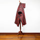 A red and black patterned poncho drapes over a wooden mannequin stand, set against a white wall and wooden floor background.