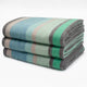 Sucua baby alpaca wool blanket – a stack of three folded, striped blankets in shades of green, blue, gray, and beige, placed against a plain white background