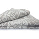 A folded blanket features a geometric pattern in shades of gray and white, resting neatly on a plain white background.