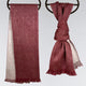 Two red scarves hang on circular holders; the left scarf drapes straight with fringed ends, while the right is artistically knotted, showcasing a lighter inner lining in a simple setting.