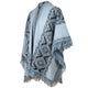 A blue poncho with geometric patterns featuring diamond shapes, finished with fringed edges. It appears draped and is displayed in a studio setting.