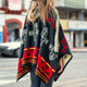 A person wearing a colorful, patterned poncho stands on a city street, with blurred buildings and a car in the background.
