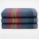 Huasaga baby alpaca wool blanket – a stack of three folded wool blankets with blue, red, and yellow stripes rests on a white surface, creating a colorful pattern against a plain background