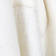A close-up image of a cream-colored, textured fabric with a visible seam, showing its soft, woven pattern, likely part of a garment, against an indistinct background.