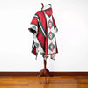 A colorful poncho with geometric patterns and a hood is displayed on a wooden stand against a plain white wall and wooden floor.