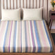 Yunga baby alpaca wool blanket – a bed is covered with a pastel-striped sheet, accompanied by two white pillows. It is situated in a room with a wooden headboard, a small nightstand, and a vase of flowers