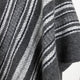 A textured fabric featuring dark gray and white horizontal stripes flows gently, creating a cozy and soft appearance. The woven pattern suggests warmth and comfort, ideal for winter garments.