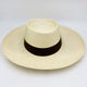 A cream-colored straw hat with a black band around the crown rests on a smooth, white surface, emphasizing its texture and classic design.