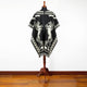 Poncho displayed on a wooden stand with rearing horses design. Situated in a room with wooden flooring and a plain white wall background.