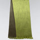 A two-toned green scarf hangs vertically, featuring smooth fabric and fringed edges. It is set against a simple light gray background, emphasizing the fabric's texture.