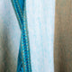 A fabric with blue and beige vertical stripes, featuring visible blue stitching, creating a textured and layered appearance. The colors blend softly, suggesting comfort and warmth.