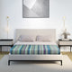 Imbabura baby alpaca wool blanket – a neatly made bed with two pillows and a colorful striped blanket; flanked by modern nightstands with lamps, under a geometric abstract artwork on a white wall