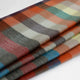 Anzu baby alpaca wool blanket – colorful plaid fabric is folded neatly, showcasing a pattern of broad, horizontal stripes in shades of orange, blue, green, gray, and cream against a plain white background