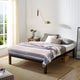 Yunga baby alpaca wool blanket – a neatly made bed with multi-colored striped blanket and pillows, positioned next to a wooden nightstand with books and a vase. A wall-mounted lamp hangs above; natural light streams from nearby window