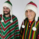 Two individuals wear colorful, striped ponchos and knitted hats with ear flaps and pom-poms, standing against a plain white background.
