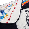 A patterned fabric shows red arrow designs and multicolored zigzags, partially covering a black and white animal depiction, set on a contrasting dark background.