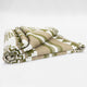 A folded blanket with green, beige, and white geometric patterns lies neatly against a plain white background.