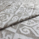 A textile blanket lies folded, featuring intricate geometric patterns in soft, muted tones. The design incorporates spirals and diamond shapes, creating a cozy and visually appealing texture.