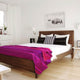 Chone baby alpaca wool blanket – a wooden bed is adorned with a bright pink striped blanket and black and white pillows, situated in a minimalistic bedroom. A bison photo hangs above, with white walls and light wood floor