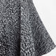 A textured fabric with a black and white speckled pattern drapes vertically, suggesting a garment or textile, against a plain white background. There is no text present.