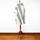 A poncho with black geometric patterns drapes over a wooden stand, set against a white wall and wooden floor.