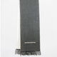 A two-toned scarf with fringe hangs vertically. The front is gray with an intricate white embroidered pattern near the bottom, against a light background.