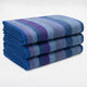 Morona baby alpaca wool blanket – a neatly folded stack of three striped blankets, featuring shades of blue, purple, and gray, resting on a plain, light-colored surface