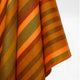 Putumayo baby alpaca wool blanket – fabric drapes with wide diagonal stripes in orange, brown, and green hues, creating a visually textured pattern against a plain white background