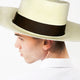 A person wearing a wide-brimmed straw hat with a dark band, looking sideways. They have a small hoop earring. The background is plain white.